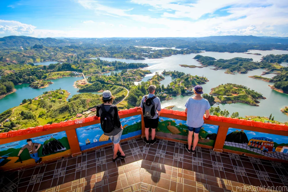 Three tourists look out over the Guatapé reservoir from El Peñol rock viewpoint in Colombia.