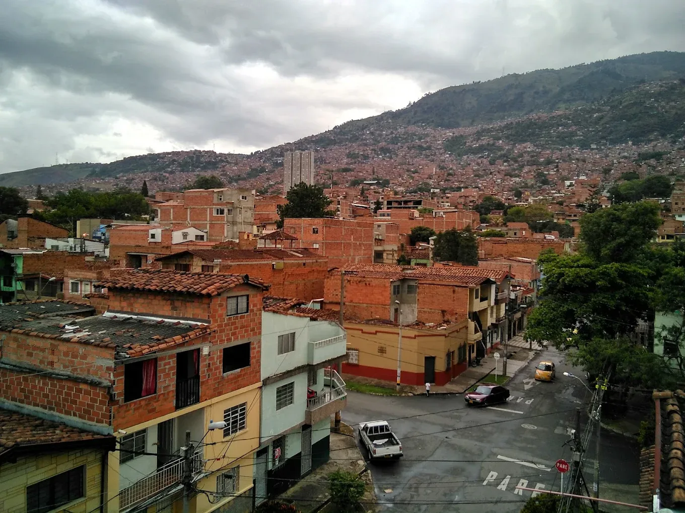 Aerial view of a red-brick neighborhood in a Latin American city with a densely populated hillside in the background.
