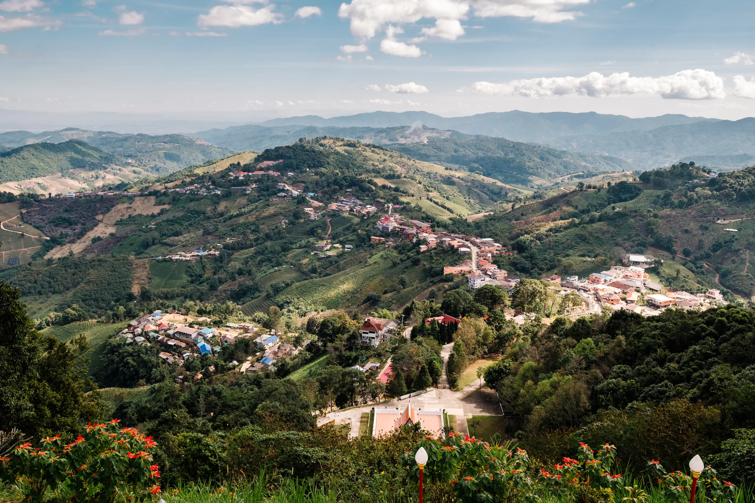 Aerial view of a small town among green hills, with red and blue roofed houses scattered through the vegetation.