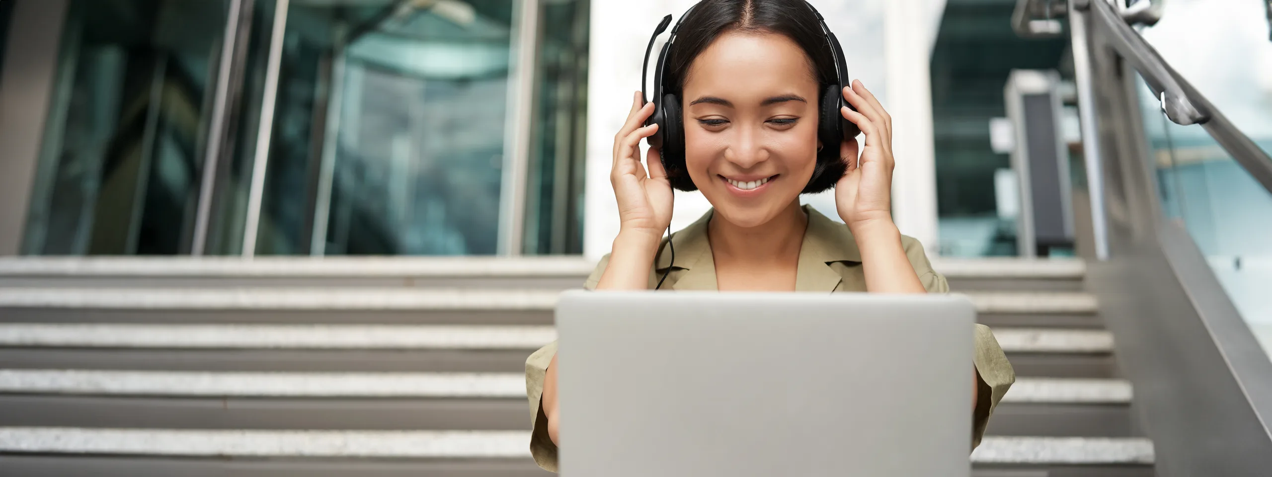 A student attending a live online Spanish class on her laptop, wearing headphones and taking notes.